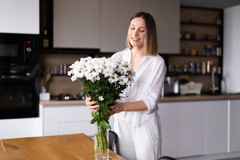 Femme heureuse qui arrange un bouquet de fleurs blanches dans sa cuisine propre