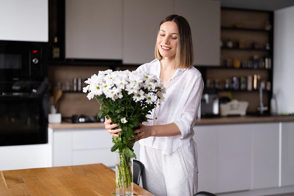Femme heureuse qui arrange un bouquet de fleurs blanches dans sa cuisine propre